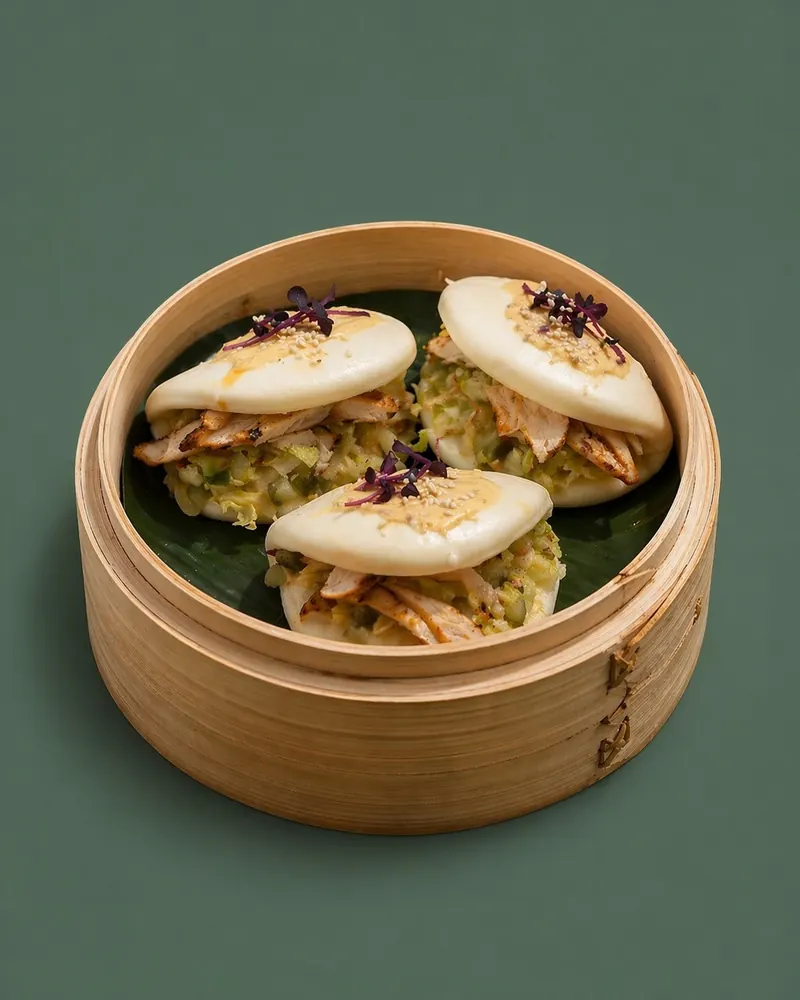 Three chicken bao buns in a bamboo steamer