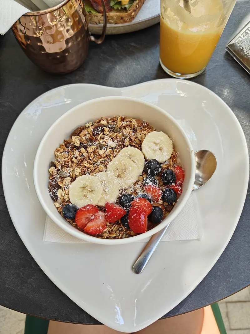 Granola bowl with banana, berries and coconut on a heart-shaped plate, with orange juice