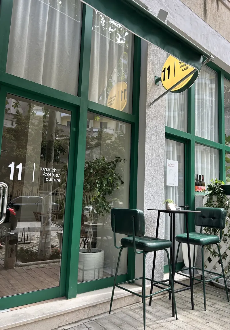 The green storefront of 11 brunch coffee culture on Rruga Cajupi, with its round yellow sign