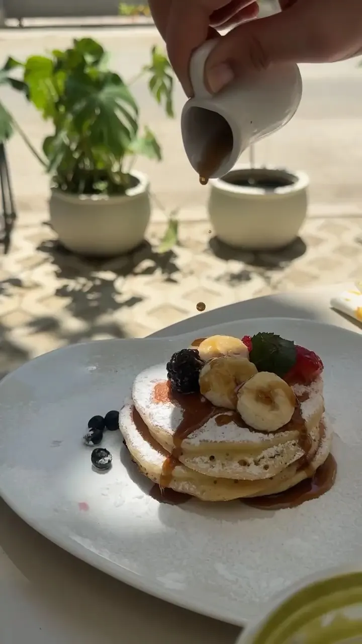 Maple syrup poured over pancakes with banana and berries